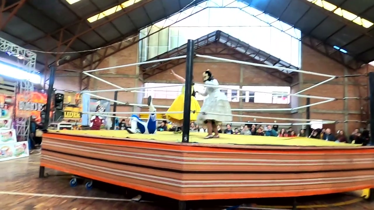 Cholita Wrestling ringinde iki güreşçi ve hakem, güreş anı
